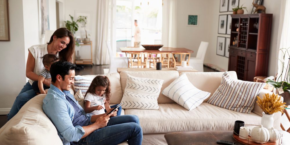 Young Hispanic family sitting on sofa reading a book together in their living room